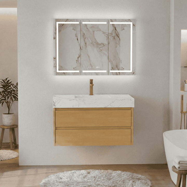Floating light wood bathroom vanity with two drawers, white marble countertop, brass faucet, and an LED mirror cabinet in a modern bathroom