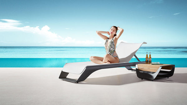 Modern outdoor lounger with side table set by poolside overlooking ocean view
