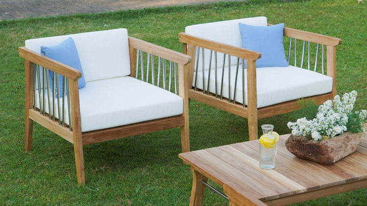 Pair of teak outdoor club chairs with white cushions and blue pillows on green lawn